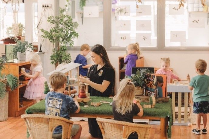 A woman is sitting at a table with children in a classroom.