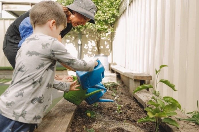 A woman and a young boy are watering plants in a garden.