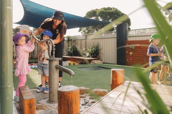 A group of children are playing with a water pump in a playground.