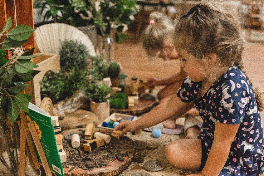 Two little girls are playing with wooden toys on the floor.