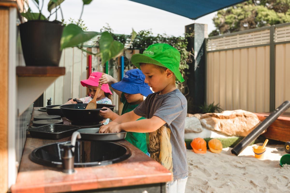 A group of children are playing in a kitchen in the sand.