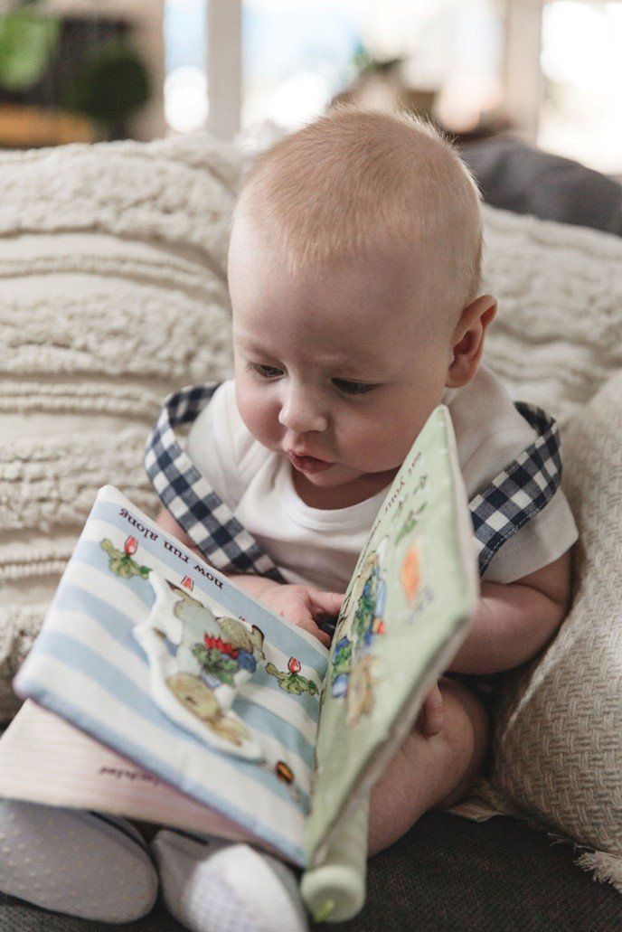 A baby is sitting on a couch reading a book.