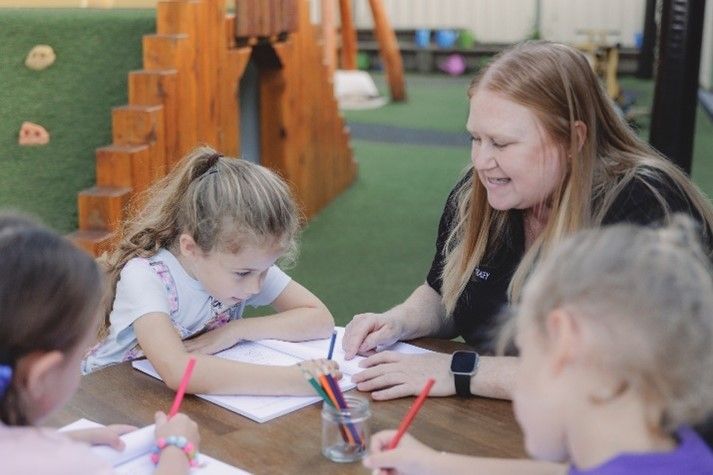 A woman is sitting at a table with a group of children.