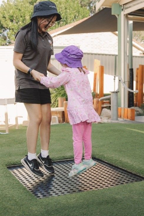 A woman is helping a little girl jump on a trampoline.