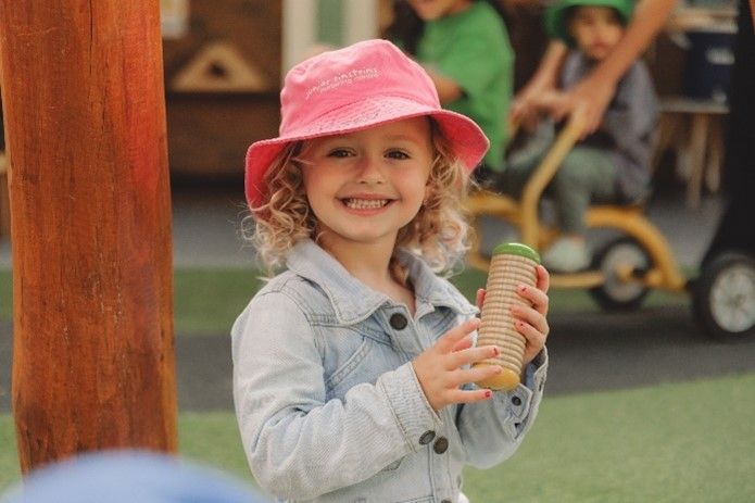 A little girl wearing a pink hat is holding a green object.