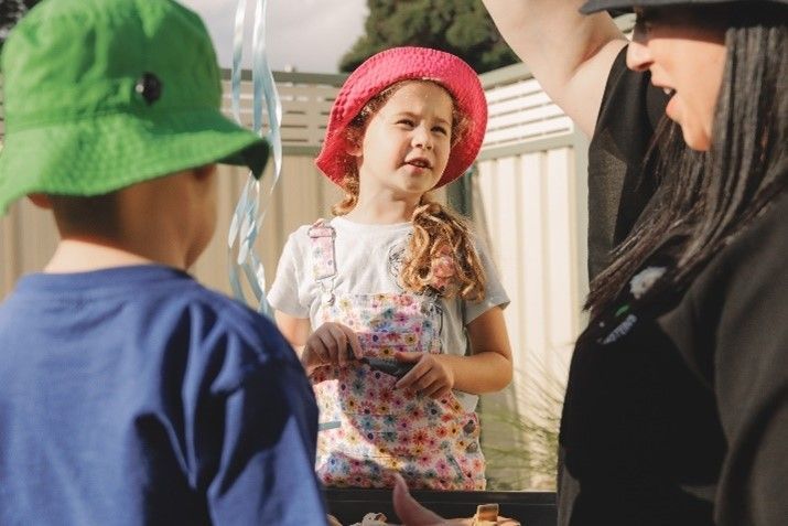 A woman is standing next to two children wearing hats.