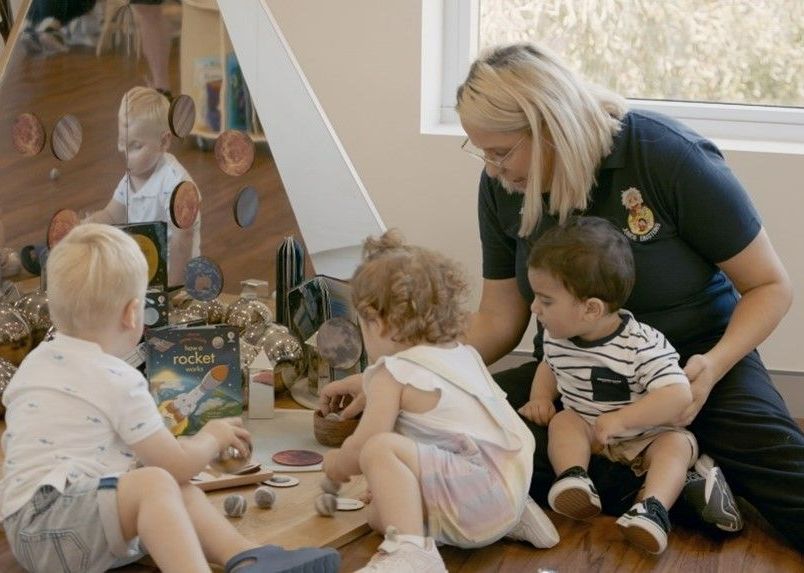 A woman is sitting on the floor playing with three children.