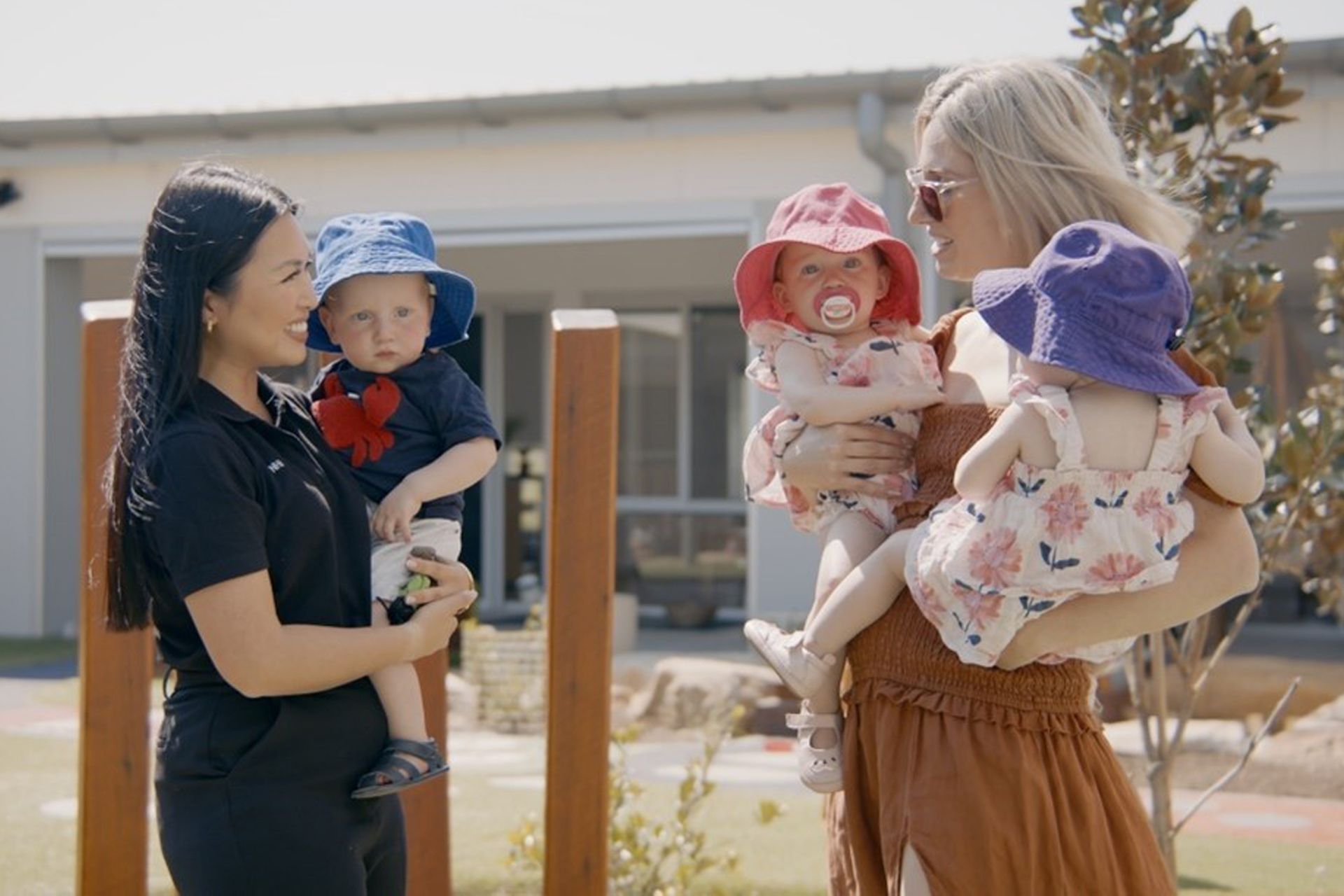 A woman is holding two babies and talking to another woman.
