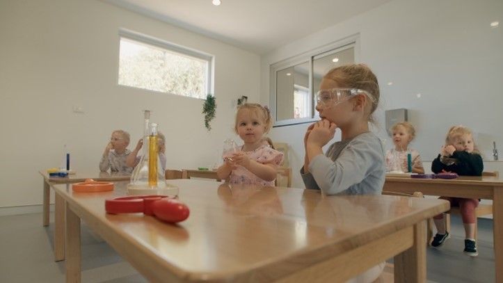 A group of children are sitting at tables in a classroom.