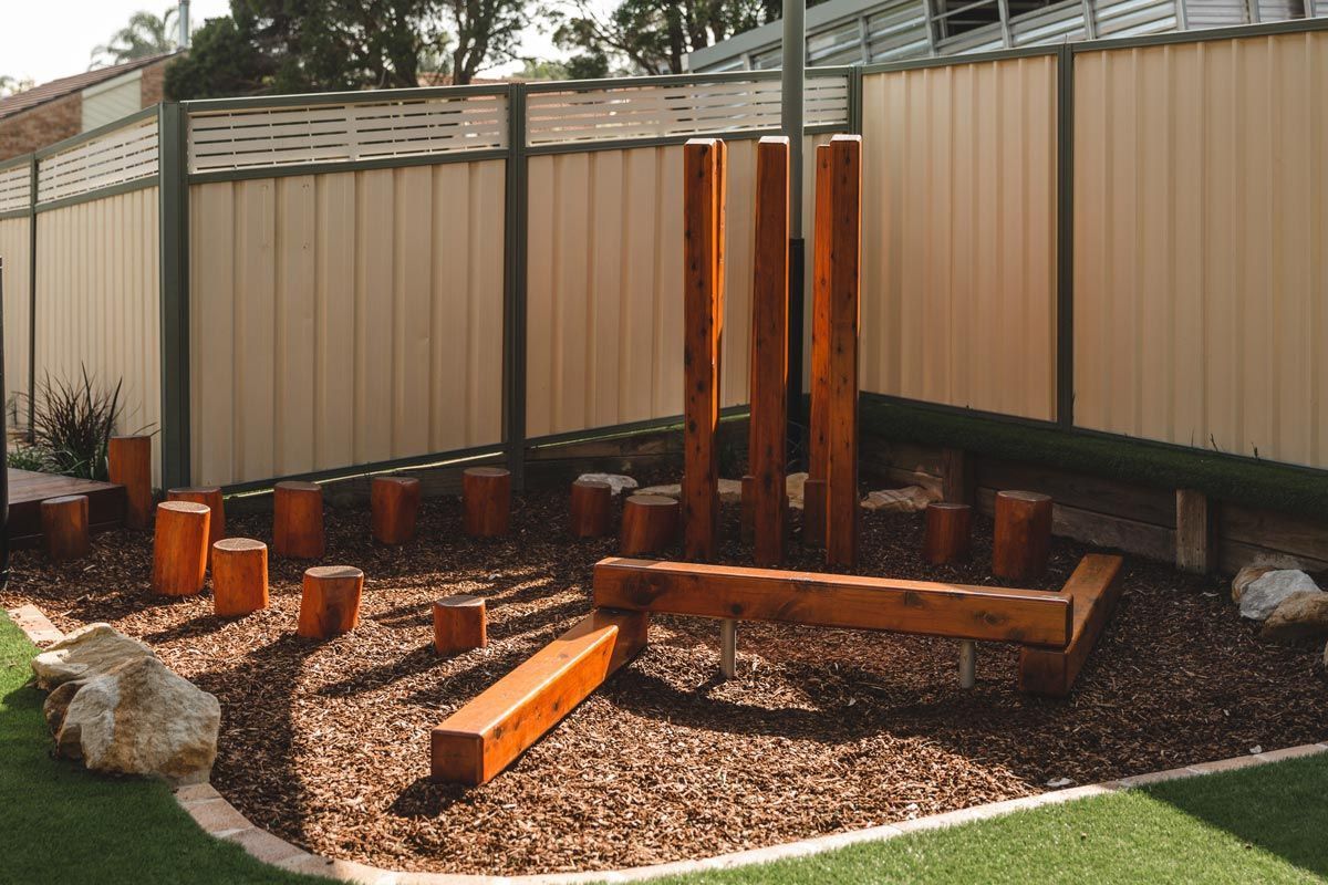 A playground with wooden blocks and a fence in the background.