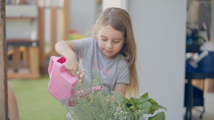 A little girl is watering a plant with a pink watering can.