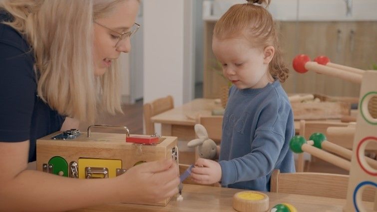 A woman and a little girl are playing with wooden toys at a table.