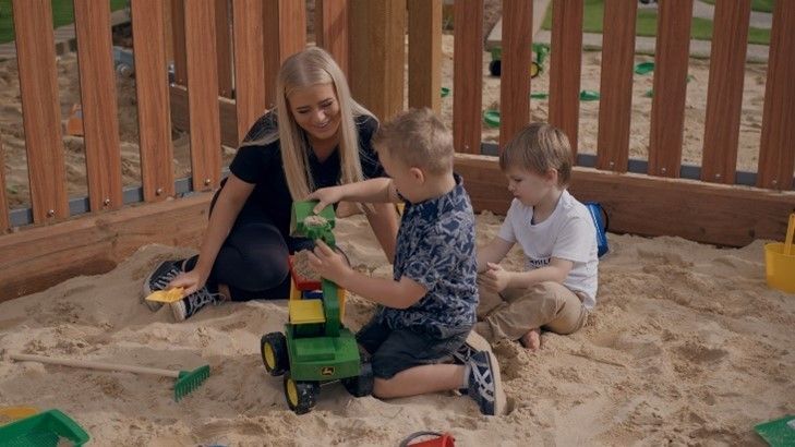 A woman is playing with two young boys in a sandbox.