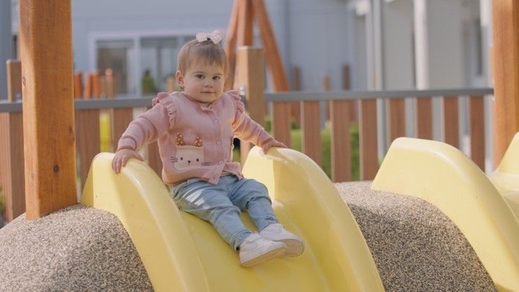A little girl is sitting on a yellow slide at a playground.