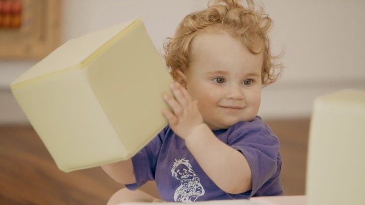 A baby is playing with a yellow foam block.
