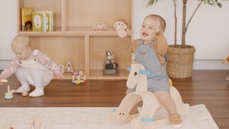 Two babies are playing with wooden toys in a living room.