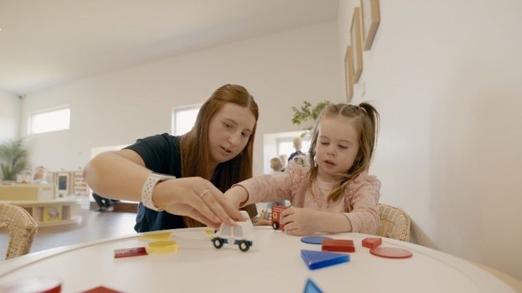 A woman and a little girl are playing with toys at a table.