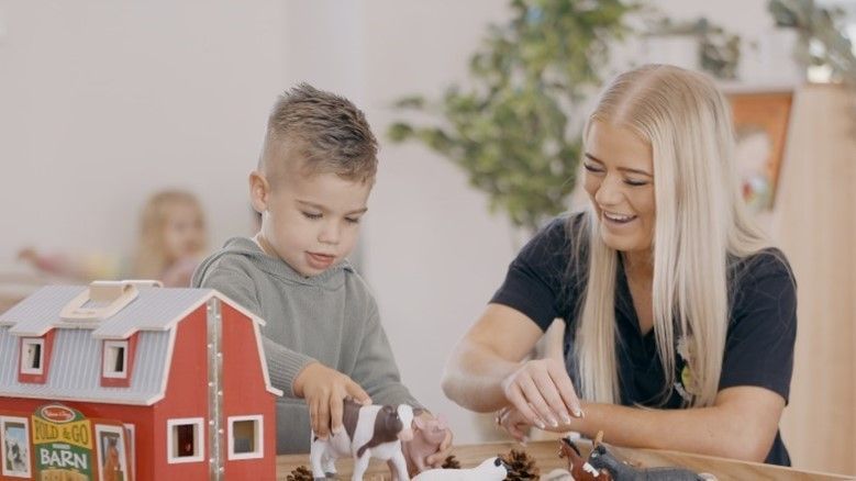 A woman and a child are playing with a toy barn.
