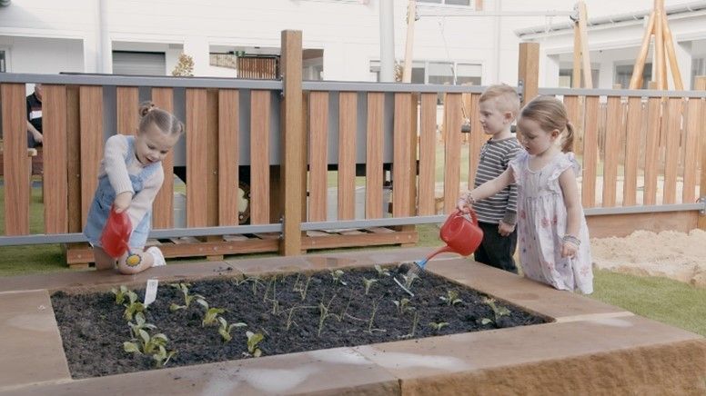 A group of children are watering plants in a garden.