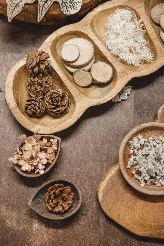 A wooden tray filled with pine cones and flowers on a wooden table.
