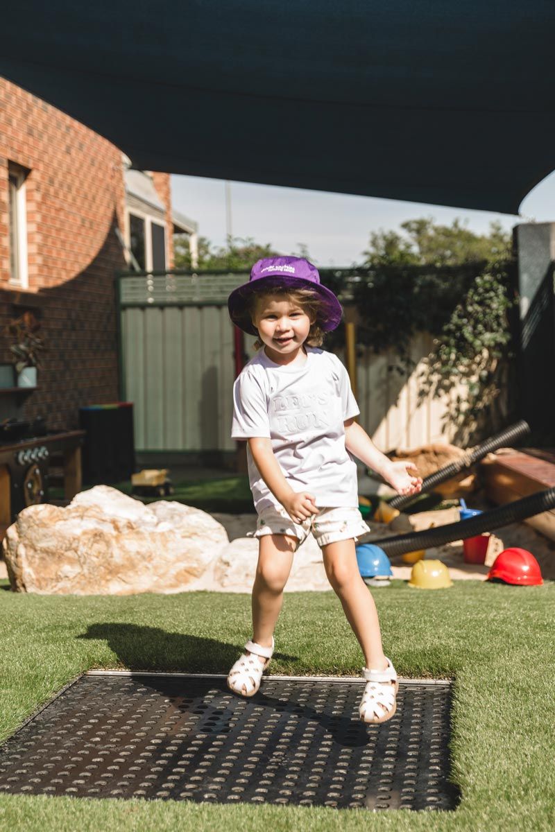 A little girl in a purple hat is jumping on a trampoline.