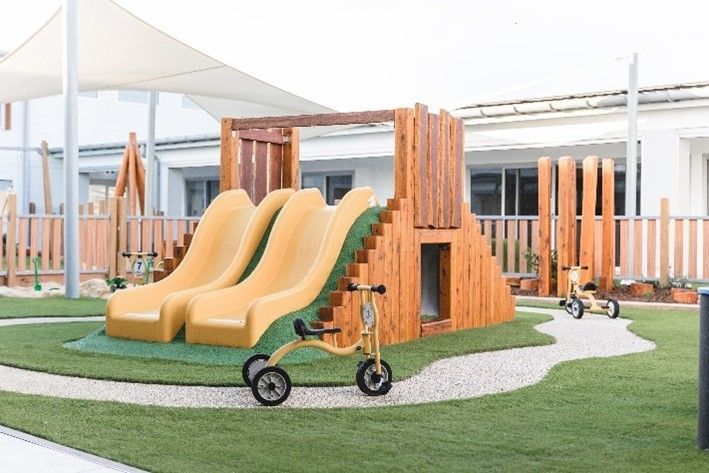 A playground with two yellow slides and a yellow tricycle.