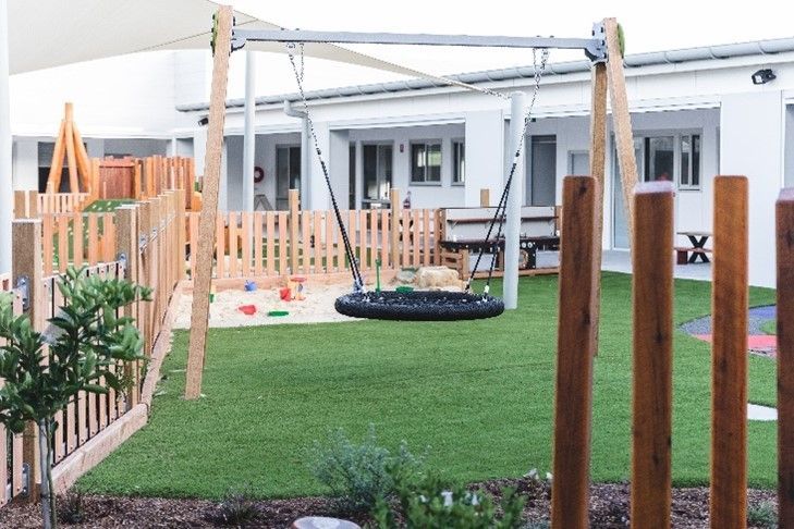A playground with a swing and a fence in front of a building.