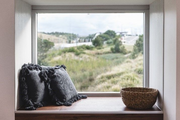 There is a window seat with pillows and a basket on it.
