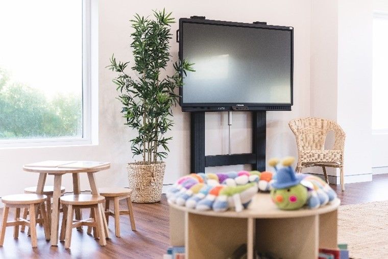 A children 's room with tables and chairs and a large flat screen tv.