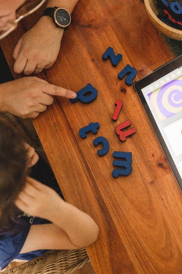 A man and a child are playing with letters on a wooden table.