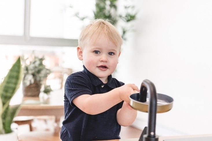 A little boy is playing with a faucet in a kitchen.