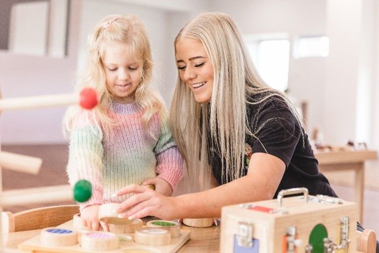 A woman and a little girl are playing with toys at a table.