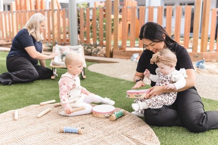 A woman is sitting on the ground holding two babies.