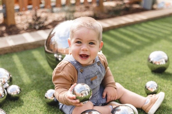 A baby is sitting on the grass holding silver balls.