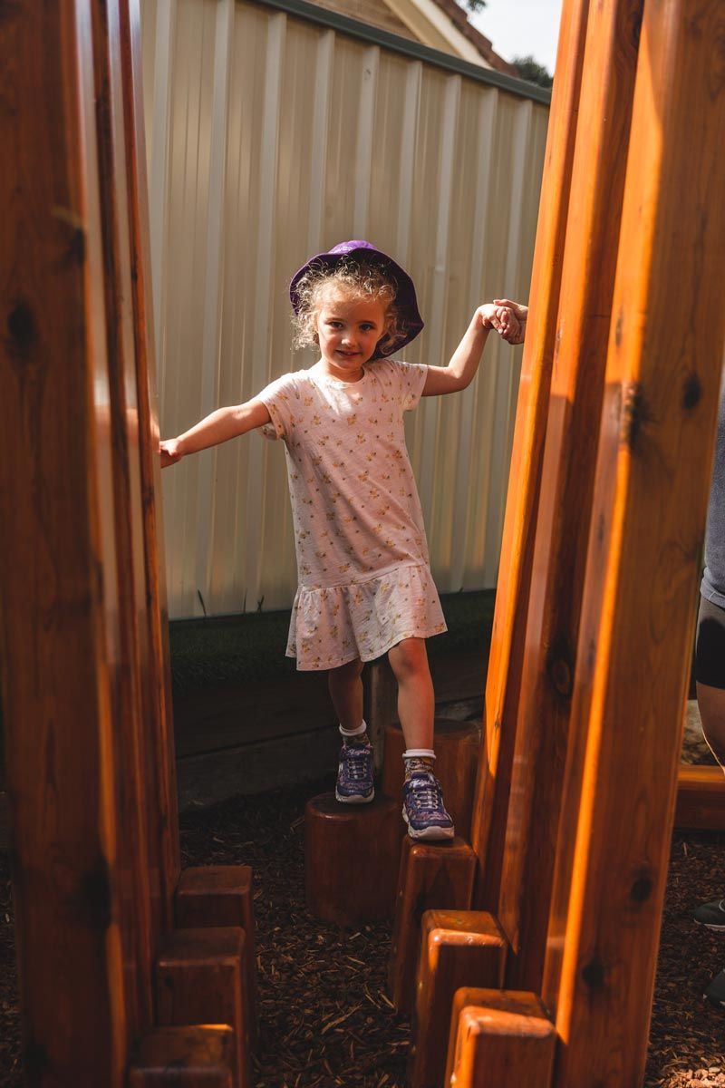 A little girl is standing on a wooden structure.