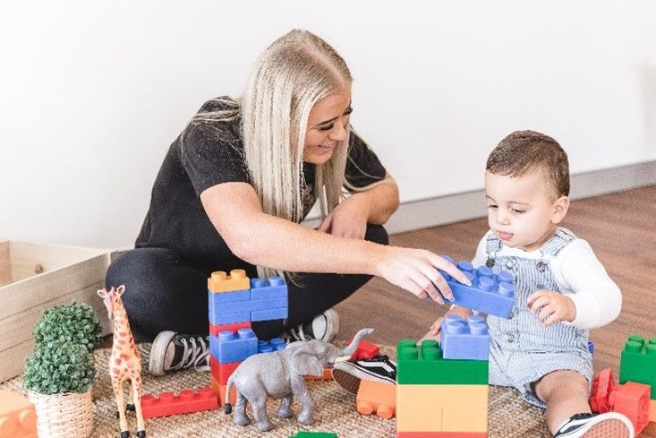 A woman and a baby are playing with blocks on the floor.