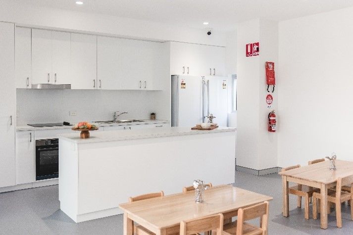 A kitchen with white cabinets and wooden tables and chairs.