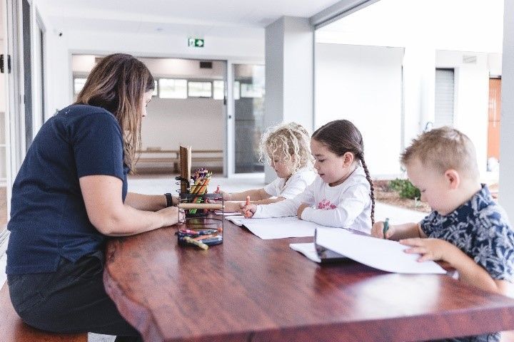 A woman is sitting at a table with three children.