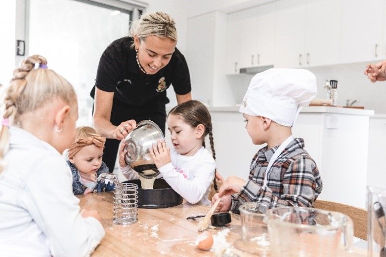 A group of children are sitting at a table with a woman in a chef 's hat.