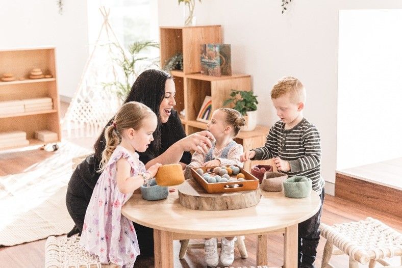 A woman is sitting at a table with three children.