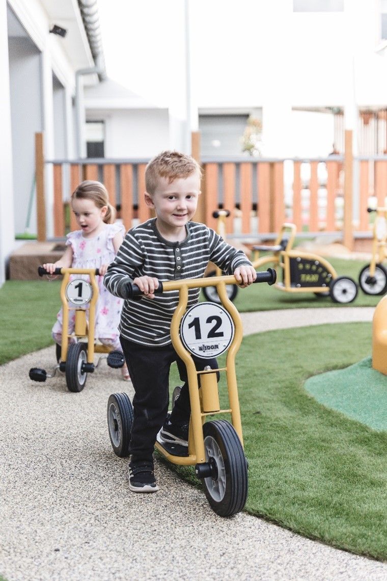 A boy and a girl are riding tricycles in a playground.