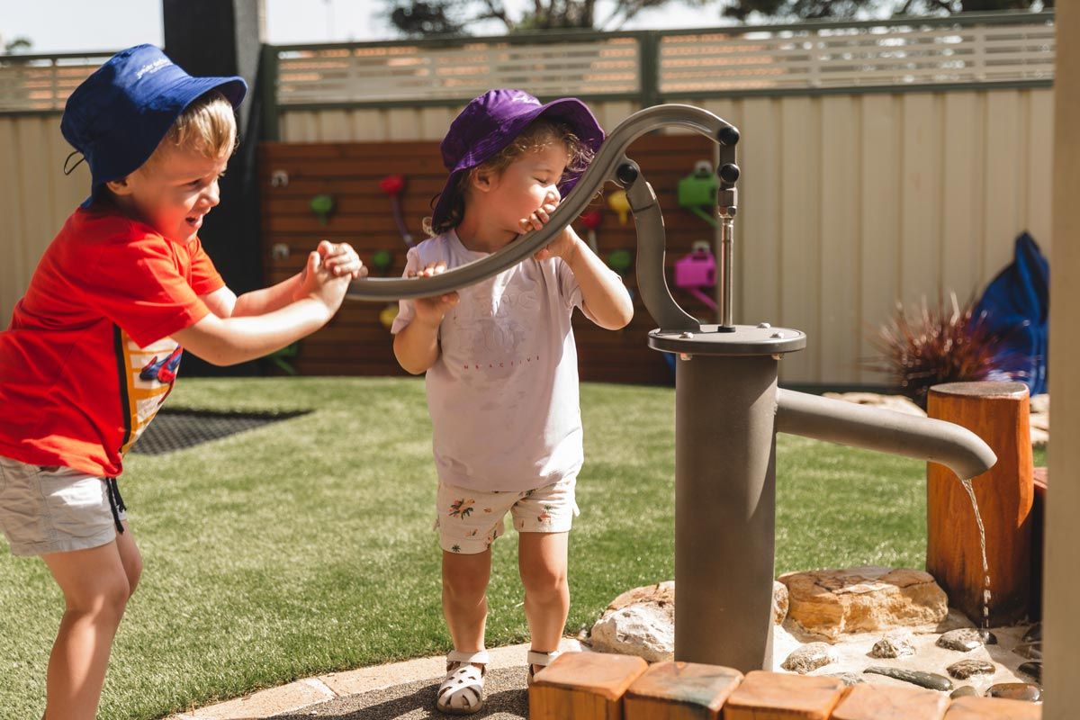A boy and a girl are playing with a water pump.