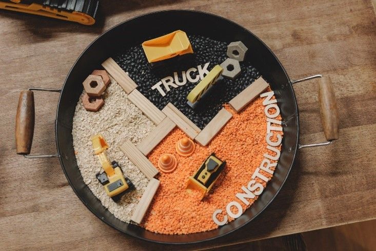 A pan filled with construction toys and rice on a wooden table.