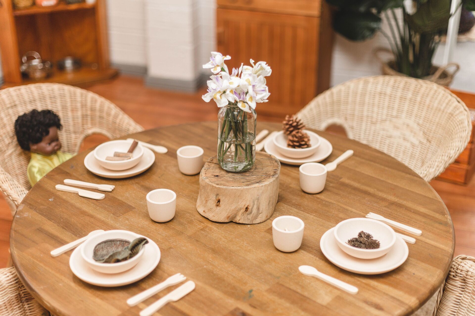 A wooden table with plates , cups , utensils and a vase of flowers on it.