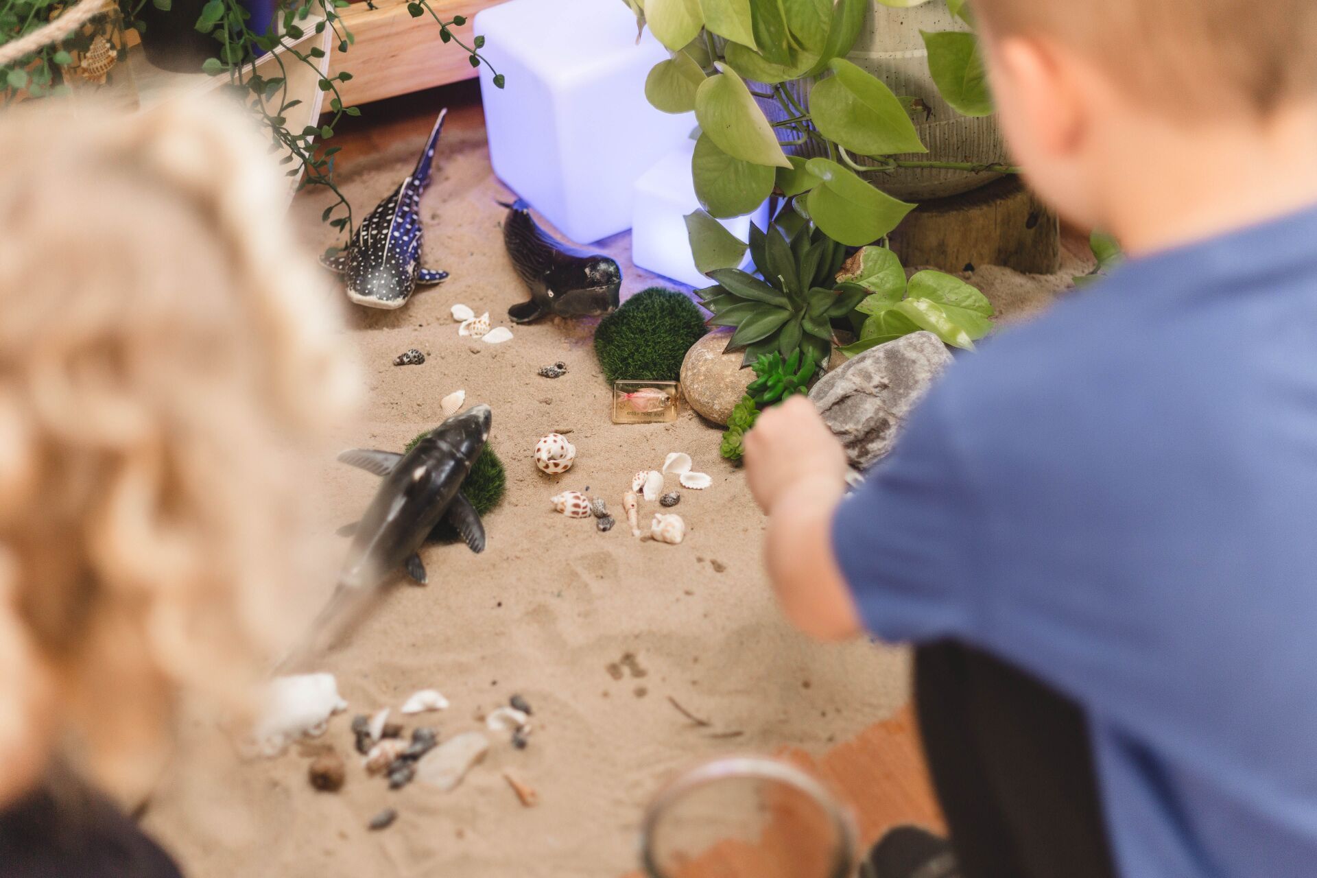 A boy and a girl are playing in the sand with dinosaurs.