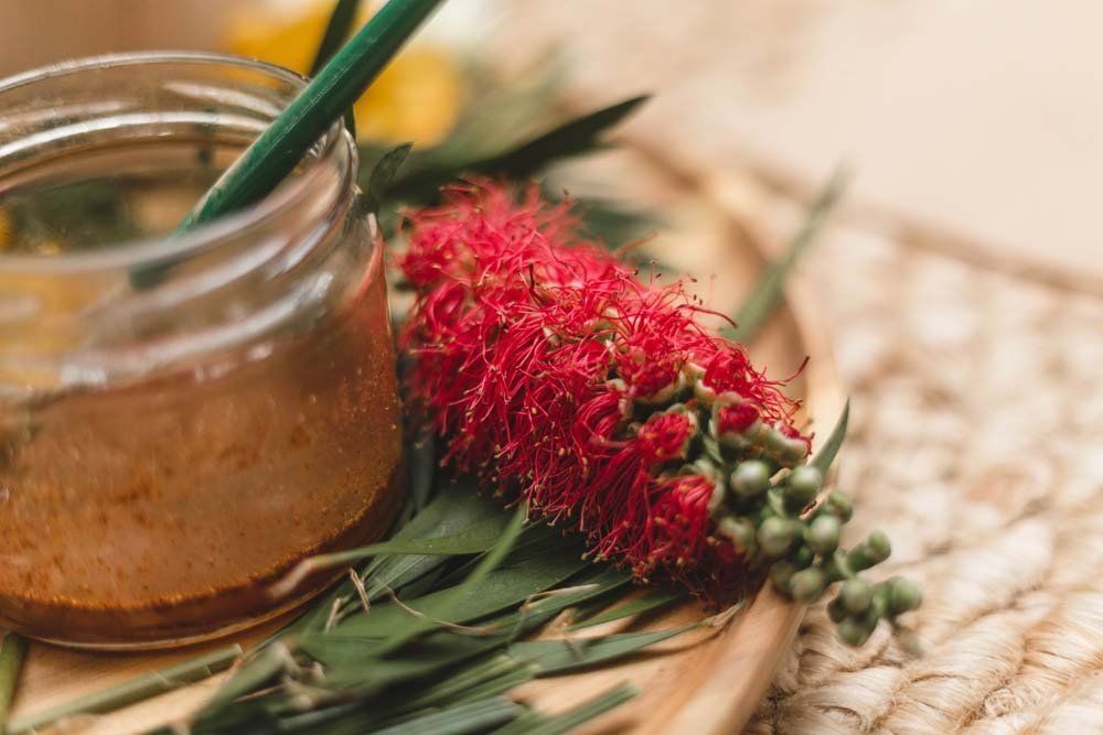A jar of honey is sitting on a wooden tray next to a flower.