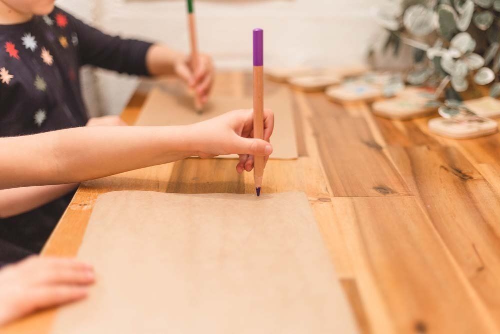 Two children are sitting at a wooden table drawing with pencils.