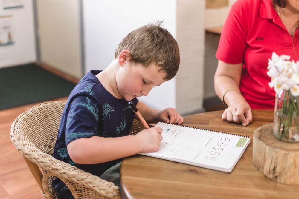 A young boy is sitting at a table writing in a notebook.