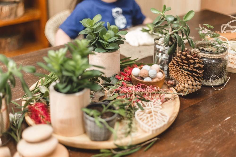 A child is sitting at a table with a tray of potted plants and flowers.