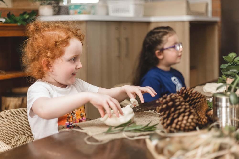 Two little girls are sitting at a table playing with pine cones.